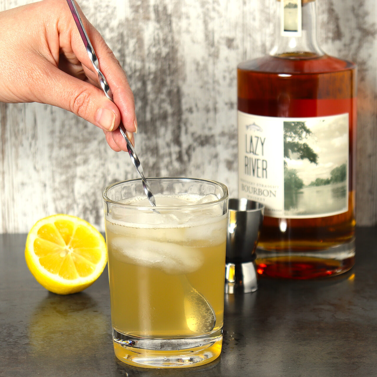 Mixing a whiskey lemonade cocktail using bourbon, lemonade, and ice.