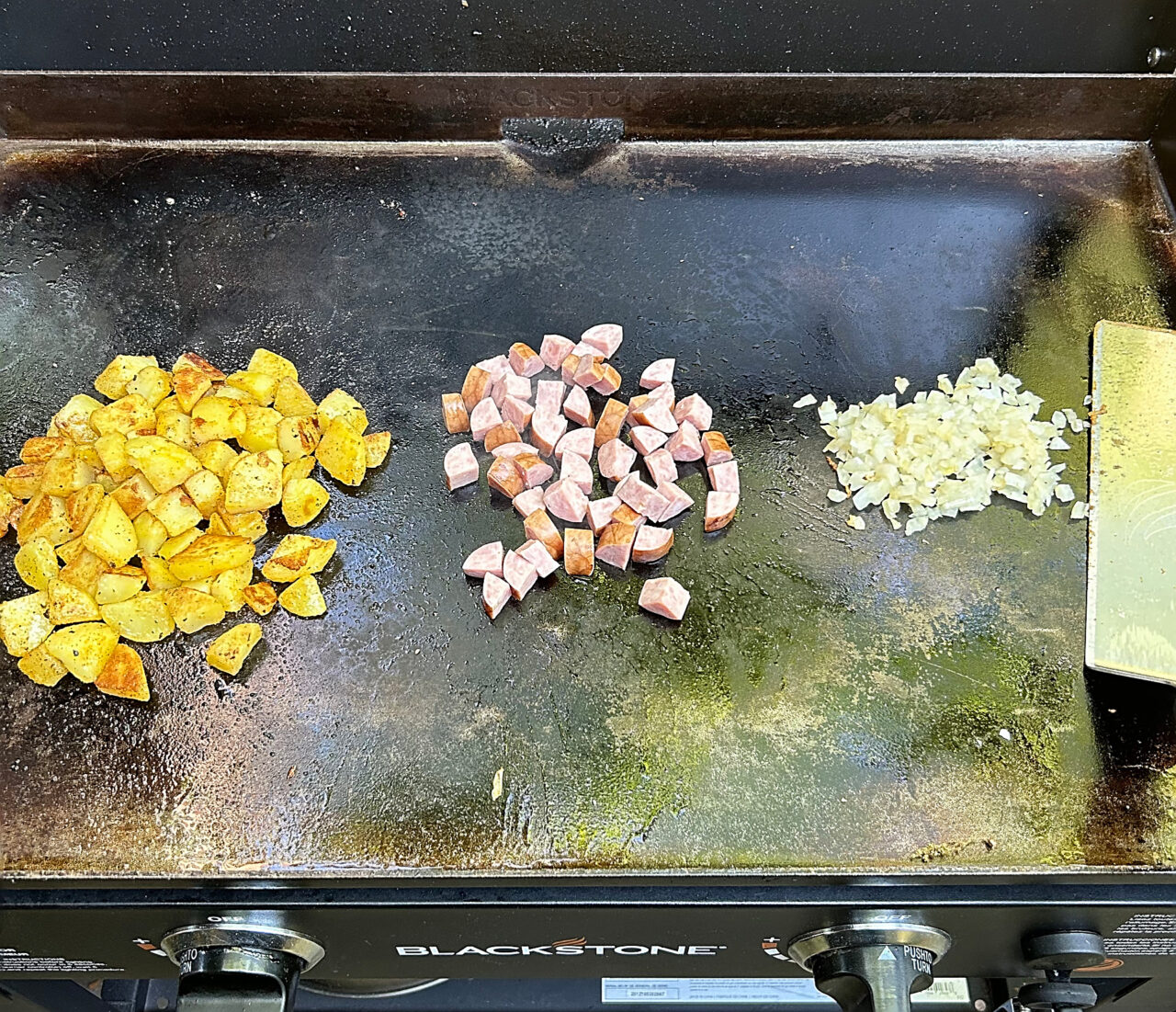 Potatoes, Kielbasa, and onions hooded on a griddle for a breakfast hash.