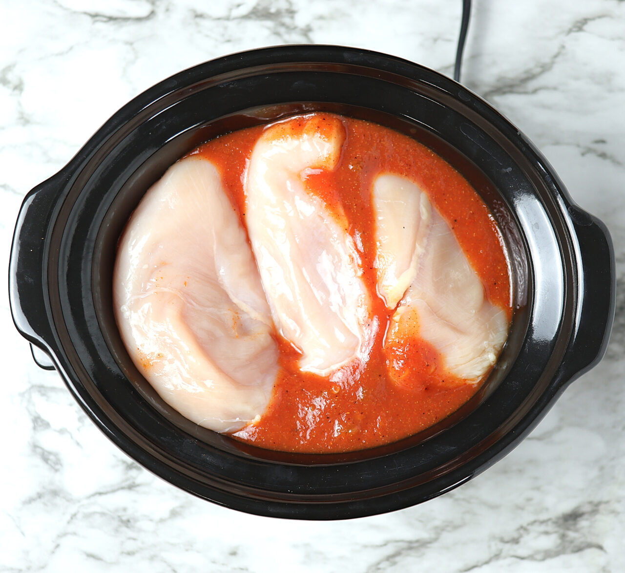 Chicken breast and homemade enchilada sauce in a crockpot.