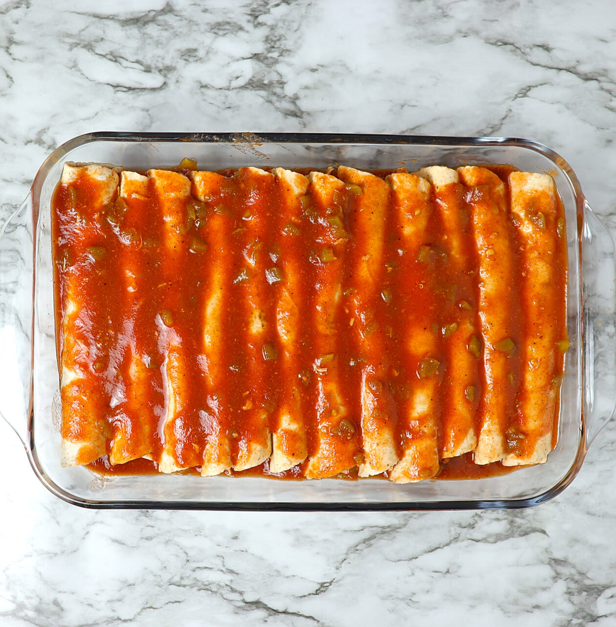 Chicken enchiladas in a glass baking dish toped with homemade enchilada sauce.