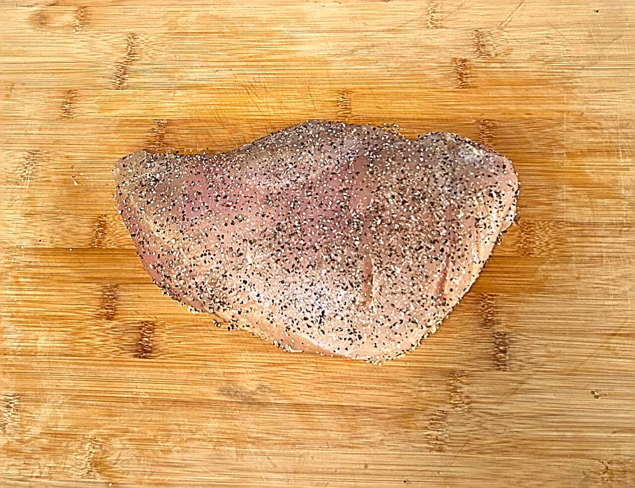 A large turkey breast seasoned with course ground pepper and kosher salt.