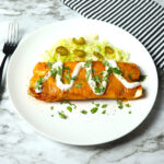 A plate of chicken enchilada topped with lettuce and sour cream.