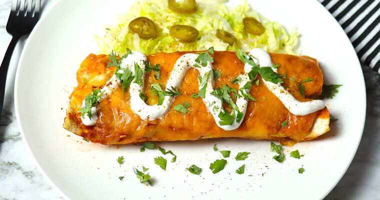 A plate of chicken enchilada topped with lettuce and sour cream.