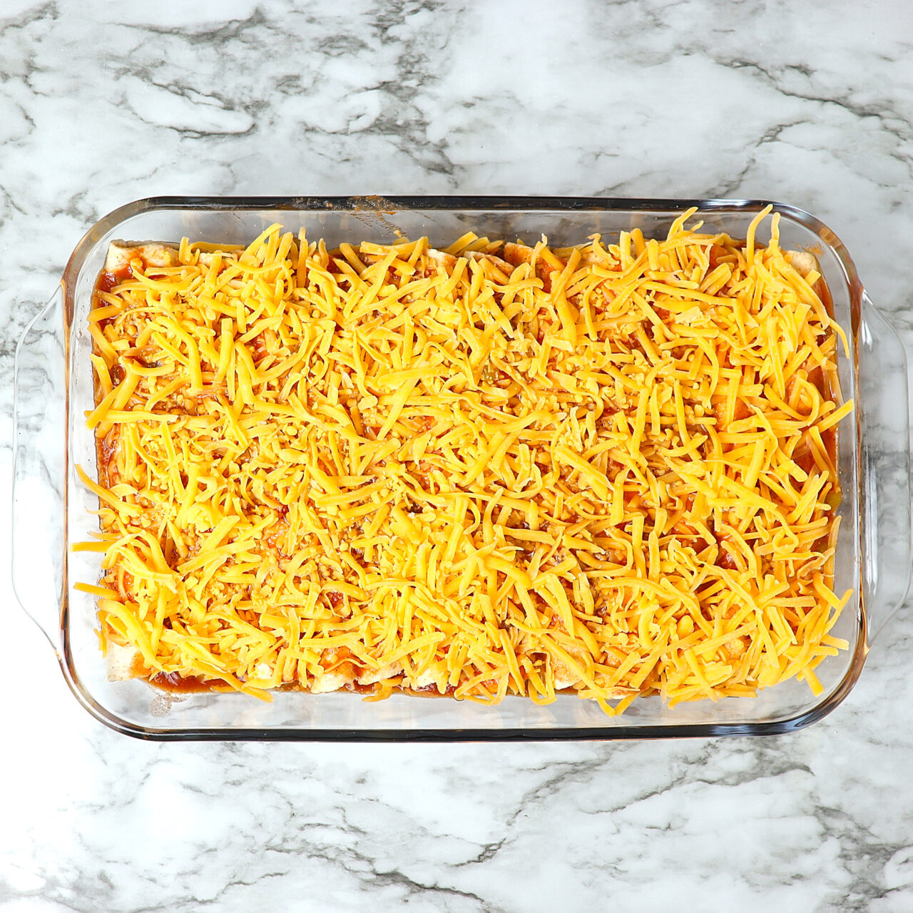 Chicken enchilada prepared in a glass baking dish topped with enchilada sauce and shredded cheese.