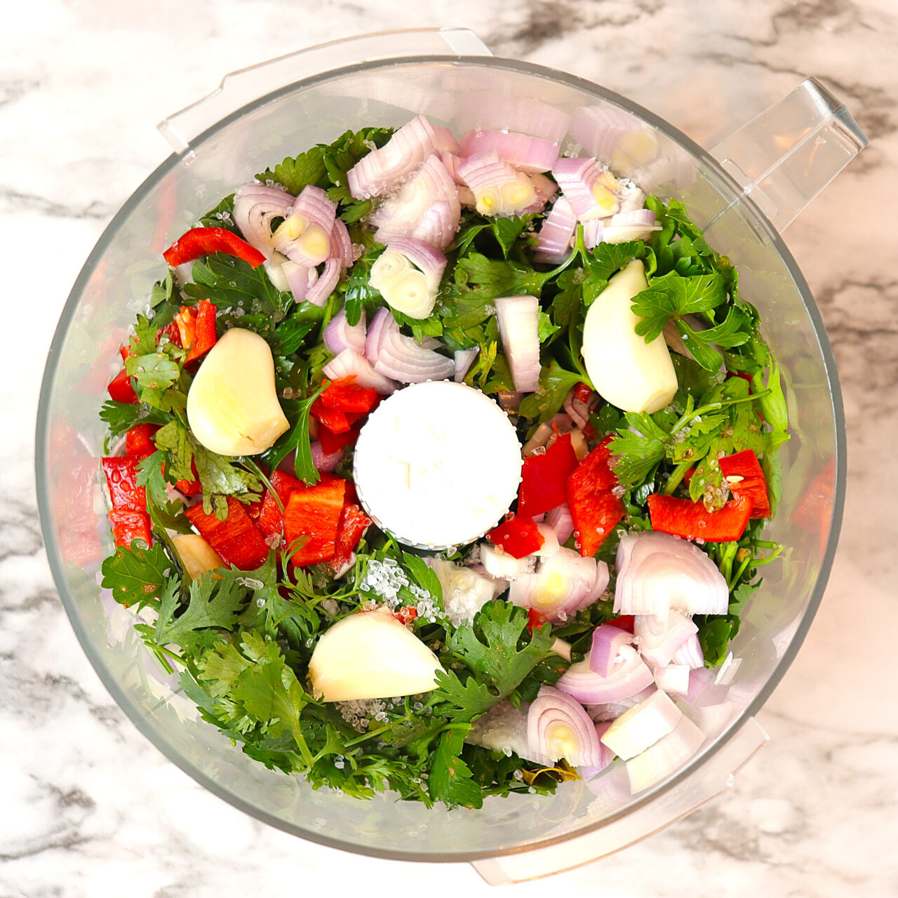 A food processor filled with fresh ingredients for a chimichurri sauce.