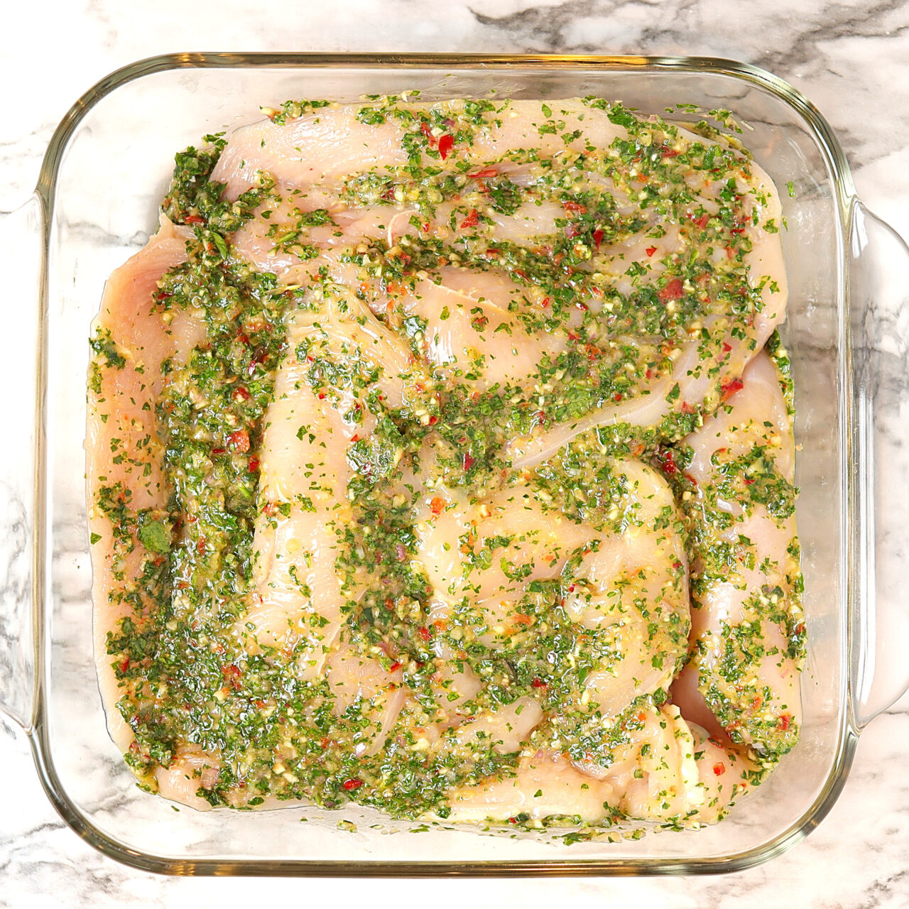 Boneless, skinless chicken breasts marinating in a fresh chimichurri sauce.