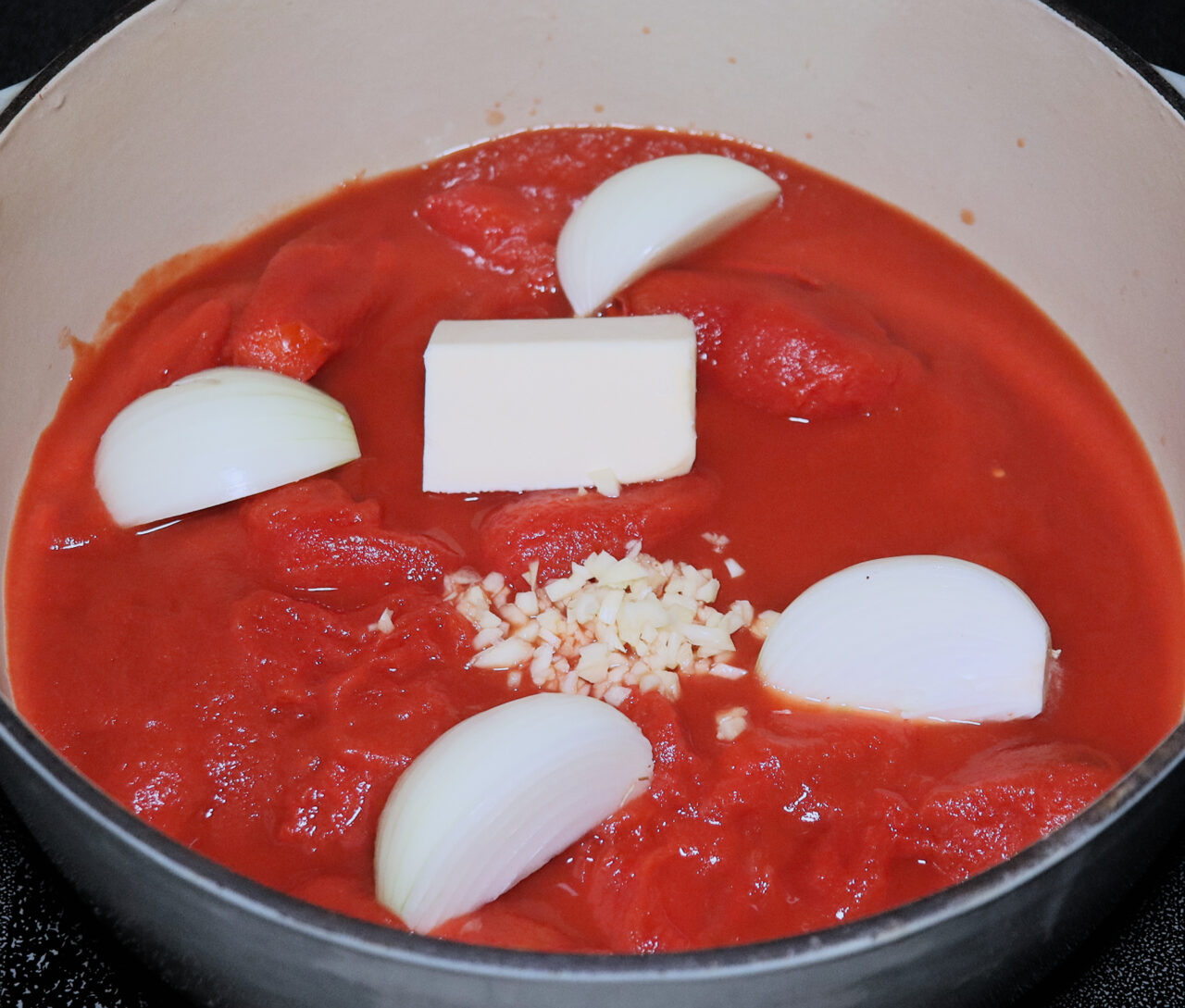 Fresh San Marzano tomatoes, quartered onions, butter, and minced garlic arranged in a pot, ready to be transformed into a flavorful homemade tomato soup.