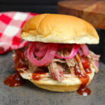 Delicious pulled pork sandwich with tender smoked pork, topped with barbecue sauce and pickled red onions, served on a soft bun.