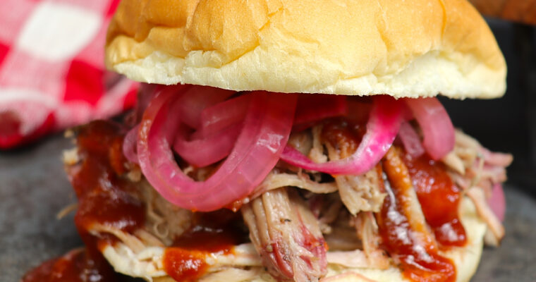 Delicious pulled pork sandwich with tender smoked pork, topped with barbecue sauce and pickled red onions, served on a soft bun.