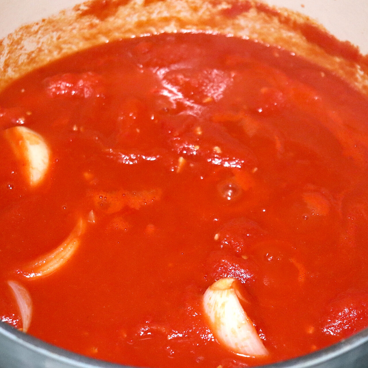 Simmering pot of San Marzano tomatoes, quartered onions, butter, and minced garlic, releasing fragrant aromas as they meld together, promising a delicious homemade tomato soup.