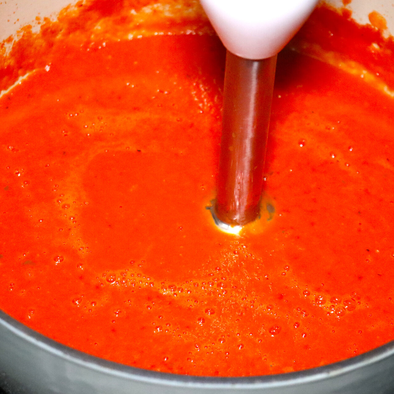 Blending the vibrant tomato soup with an immersion blender for a smooth and velvety texture, creating a luscious and satisfying culinary masterpiece.