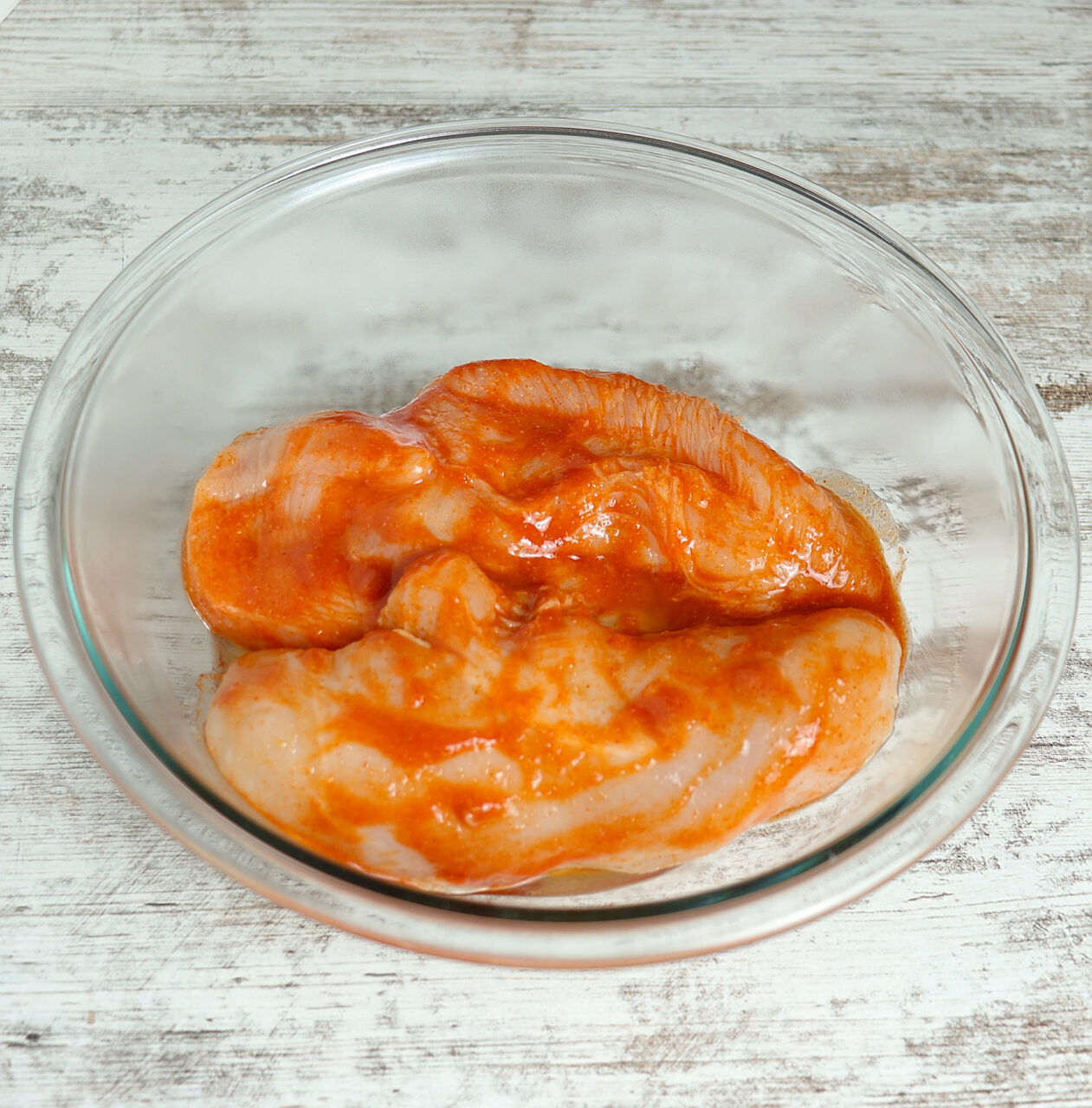 Raw chicken breasts marinating in a flavorful blend of buffalo sauce and spices, ready for grilling or cooking."