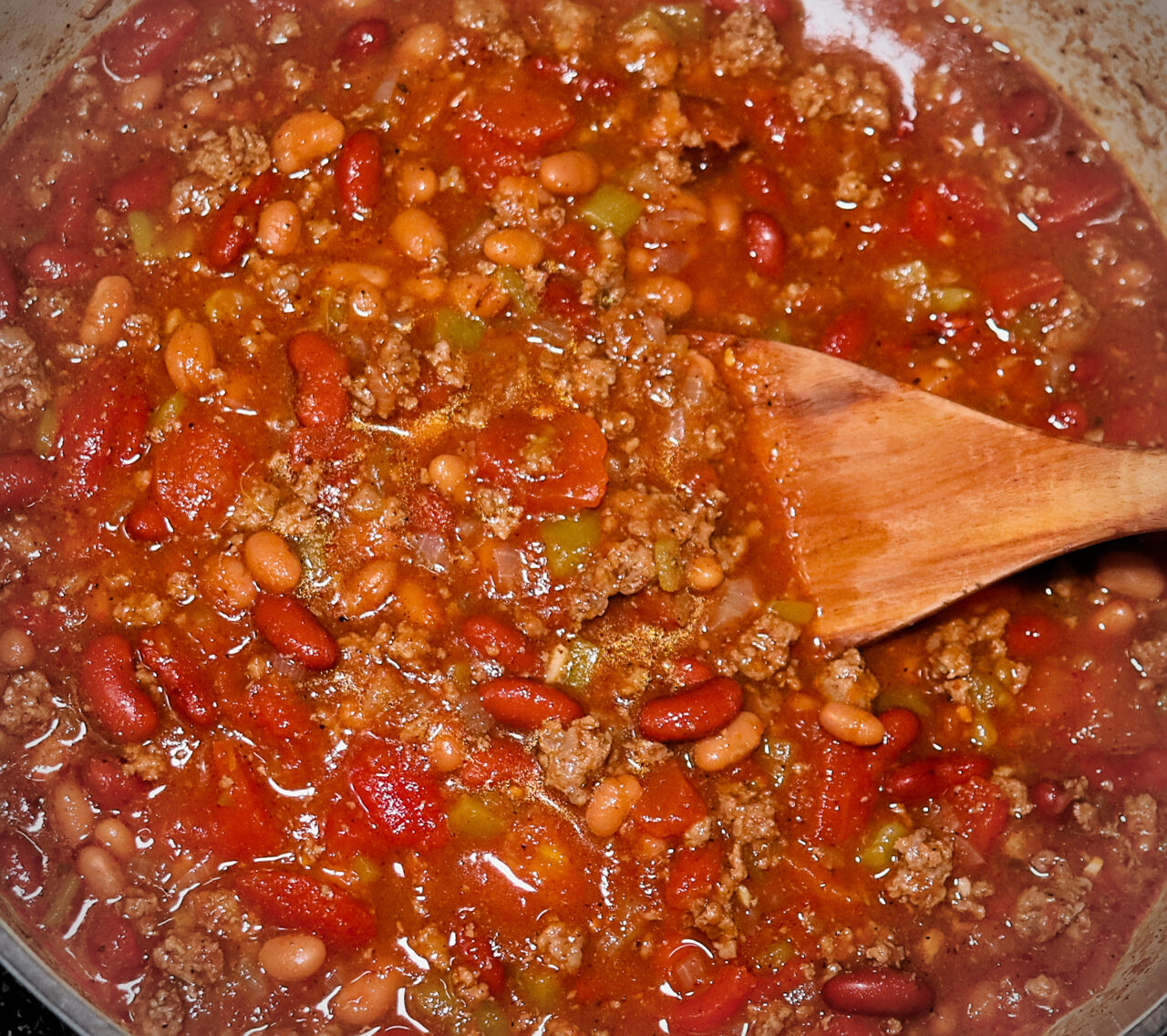 Delicious pot of chili with ground beef, beans, chilis, and spices simmering on the stove.