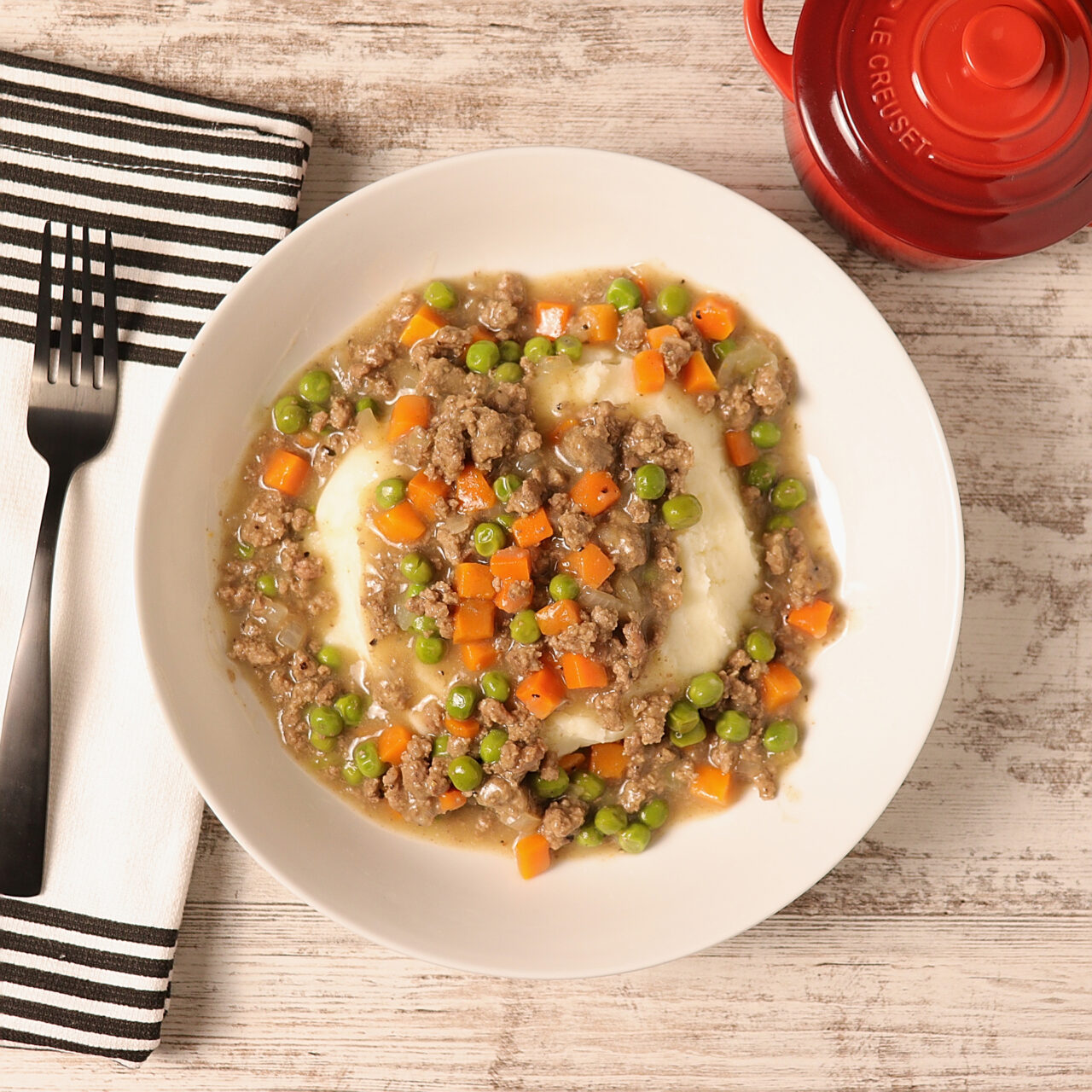 A bowl of hamburger stew with a blend of ground beef, onions, carrots, and peas served over mashed potatoes.