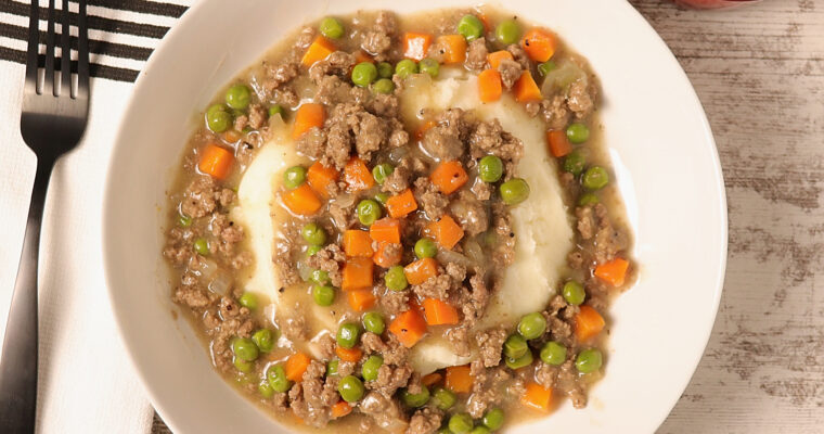 A bowl of hamburger stew with a blend of ground beef, onions, carrots, and peas served over mashed potatoes.