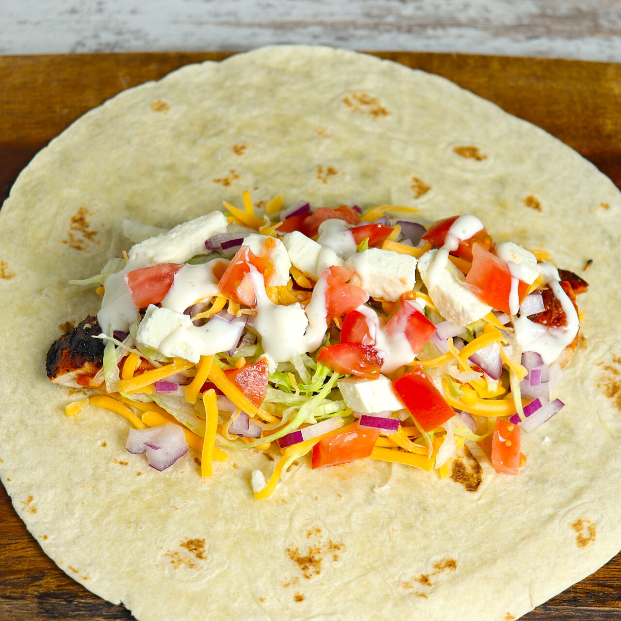 A vibrant flour tortilla filled with grilled buffalo chicken, crisp lettuce, tomatoes, and savory toppings, a delicious wrap masterpiece.