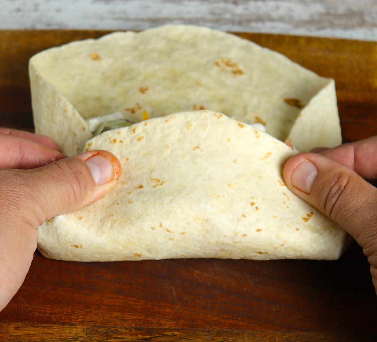 Expertly wrapping a flour tortilla around grilled buffalo chicken, fresh lettuce, tomatoes, and flavorful ingredients, creating a mouthwatering wrap.