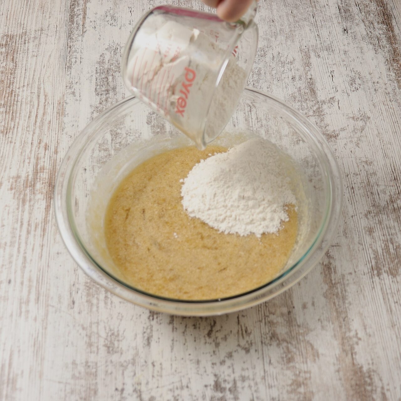 Pouring all-purpose flour into the mixing bowl of banana bread ingredients.