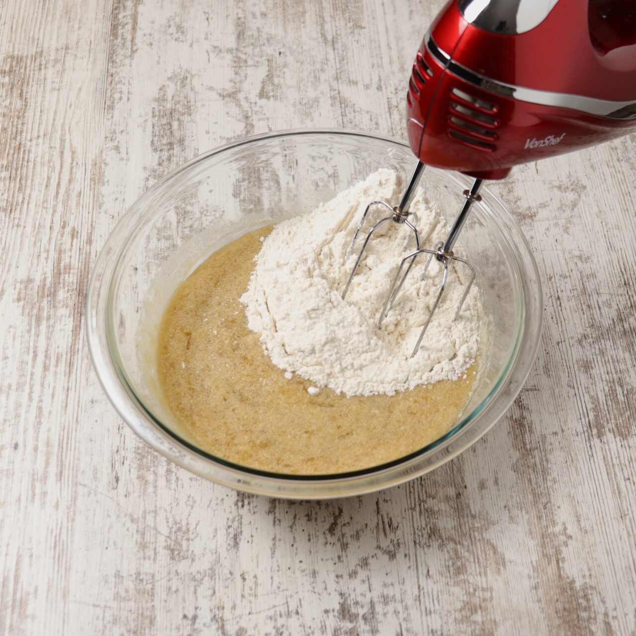 Mixing flour with an electric hand mixer into to a bowl of banana bread ingredients.