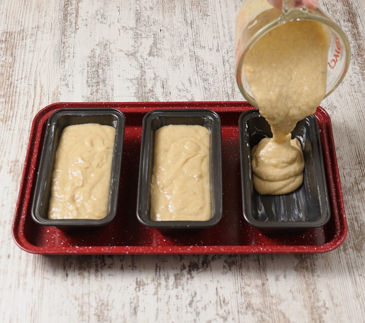 Pouring banana bread batter into baking loaf pans.