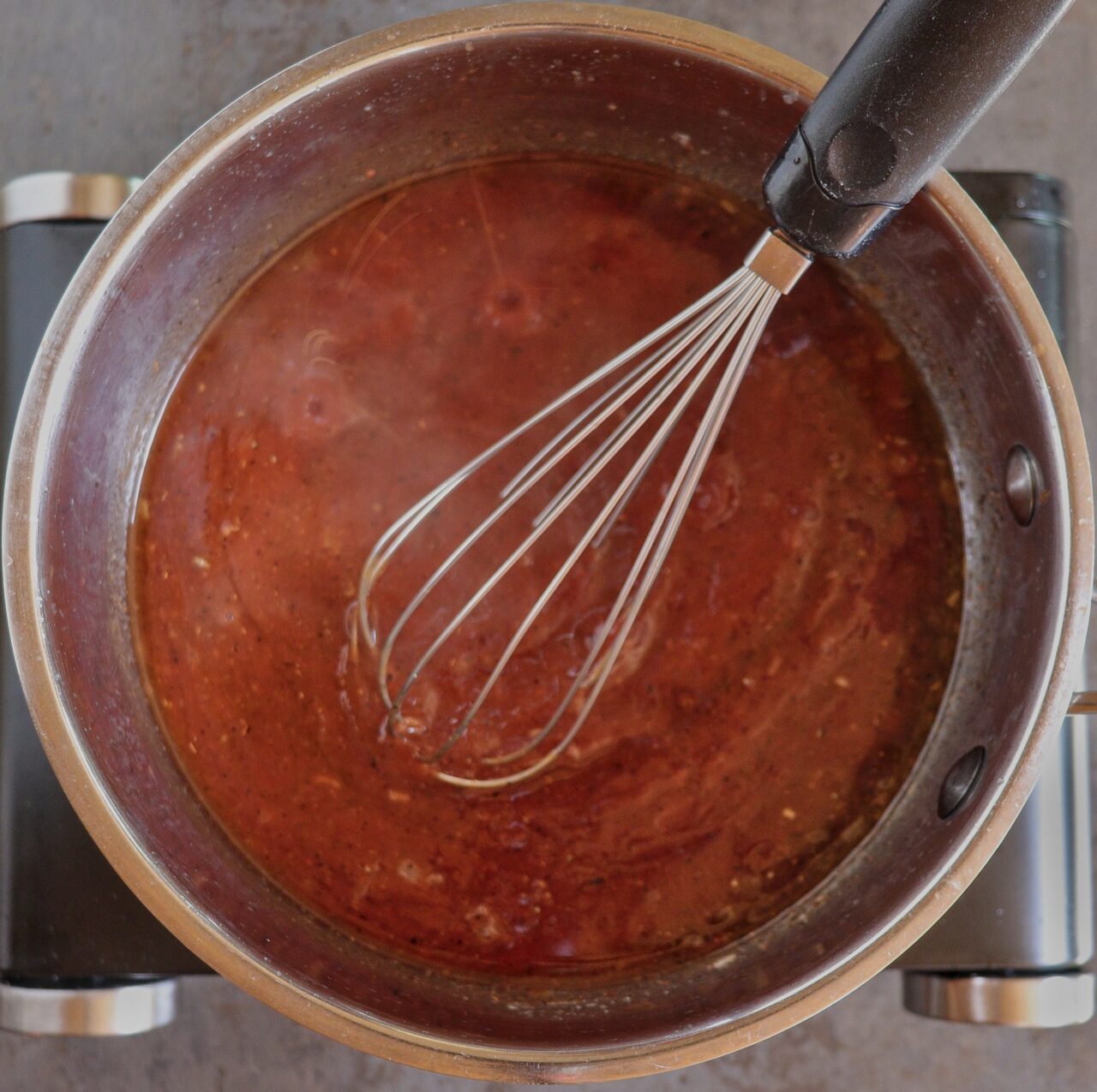 Simmering homemade BBQ sauce in a saucepan, with all ingredients combined, thickening and developing rich flavors over low heat.