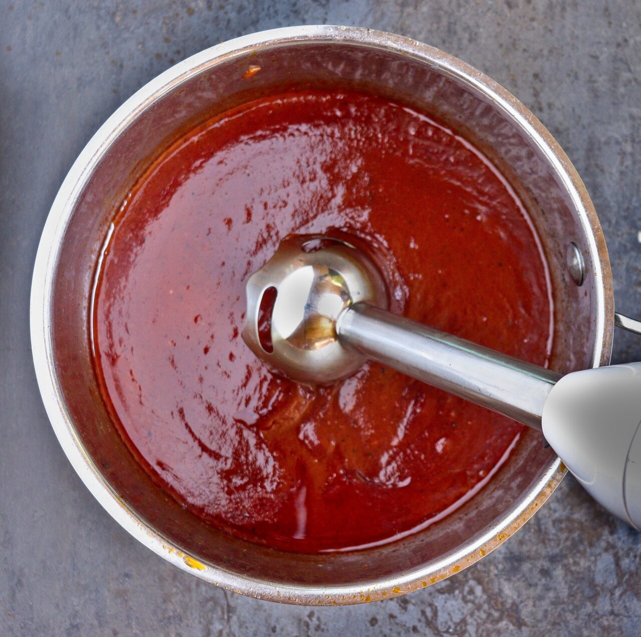 Using an immersion blender to smooth and perfect the homemade BBQ sauce, creating a silky, velvety consistency for the ideal texture.