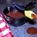 Cast iron crock filled with rich homemade BBQ sauce, with a basting brush dripping sauce over the edge—perfect for grilling ribs, chicken, or pulled pork.