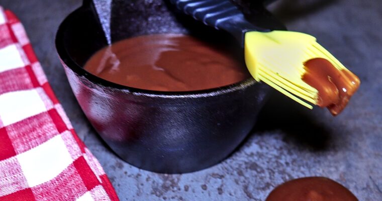 Cast iron crock filled with rich homemade BBQ sauce, with a basting brush dripping sauce over the edge—perfect for grilling ribs, chicken, or pulled pork.